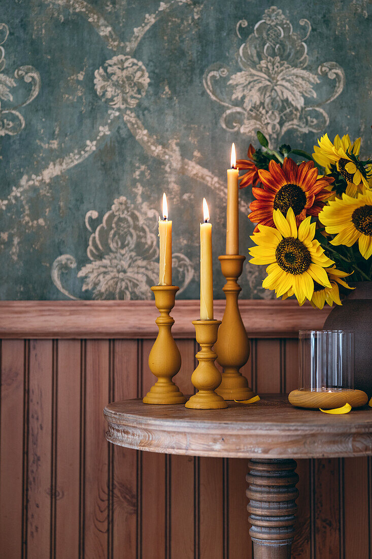 Kerzen in gelben Kerzenhaltern und Sonnenblumenstrauß auf Holztisch