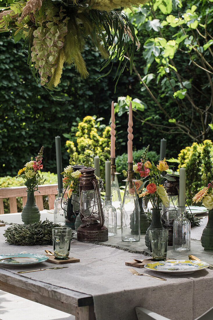 Gedeckter Gartentisch mit rustikalen Laternen, Blumendekoration und grünen Kerzen