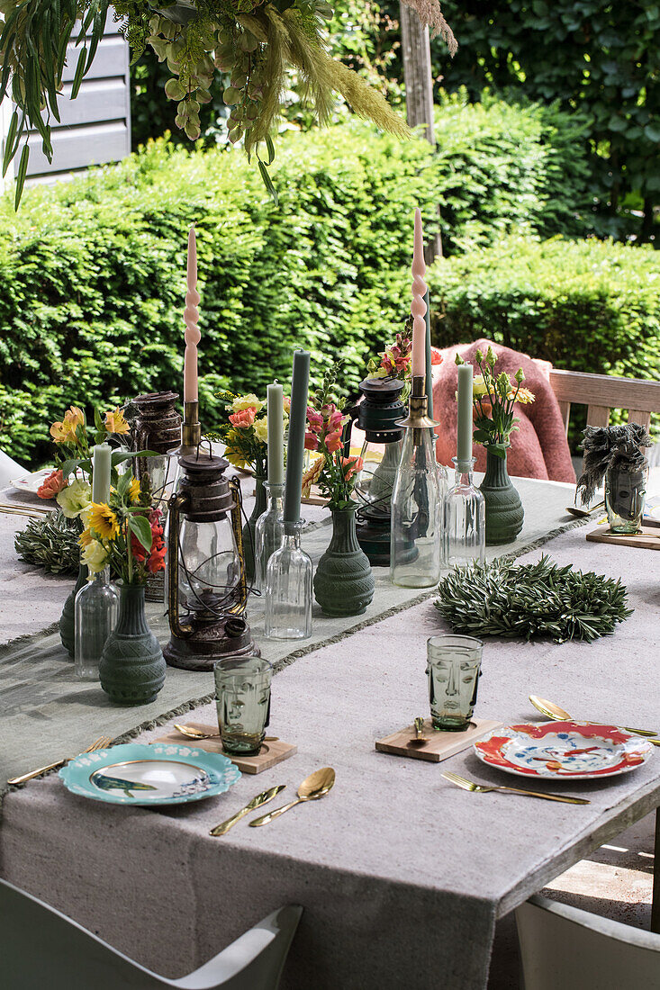 Gedeckter Gartentisch mit Kerzen, Blumen und Laternen im Sommer