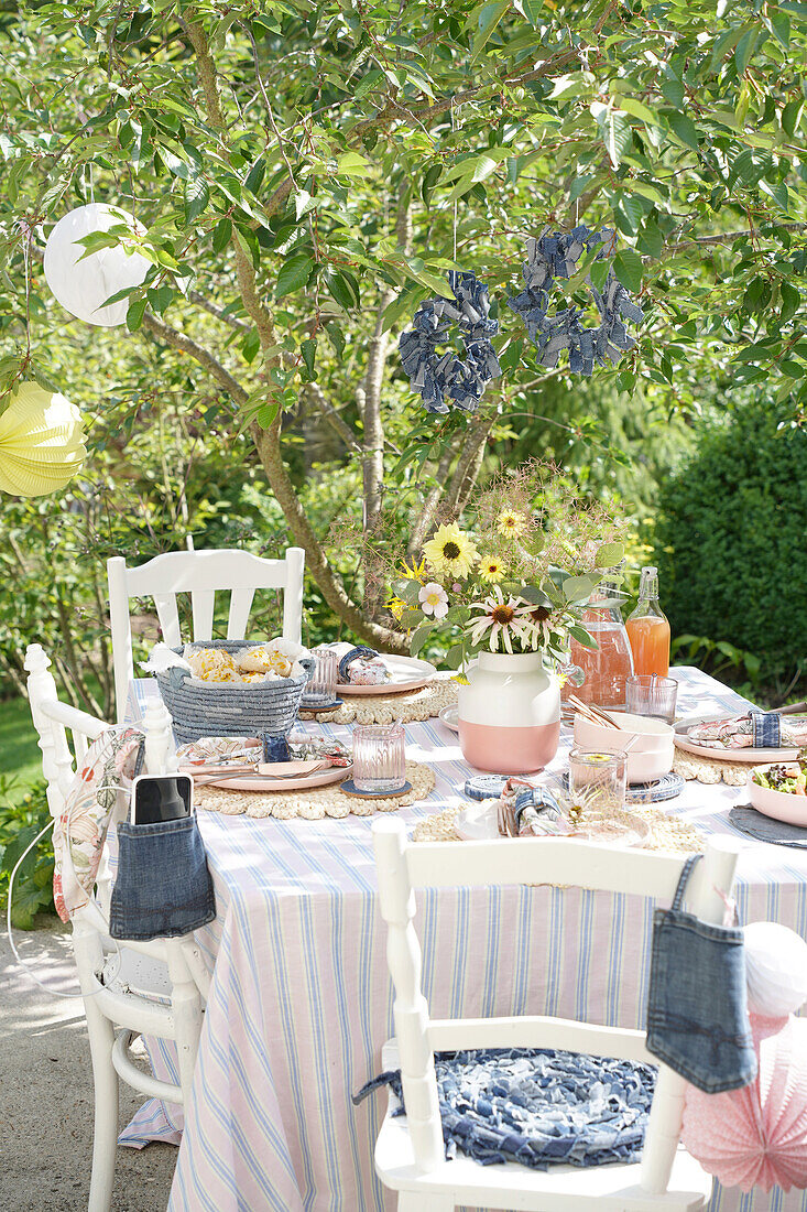 Summer table in the garden with striped tablecloth and bouquet of flowers