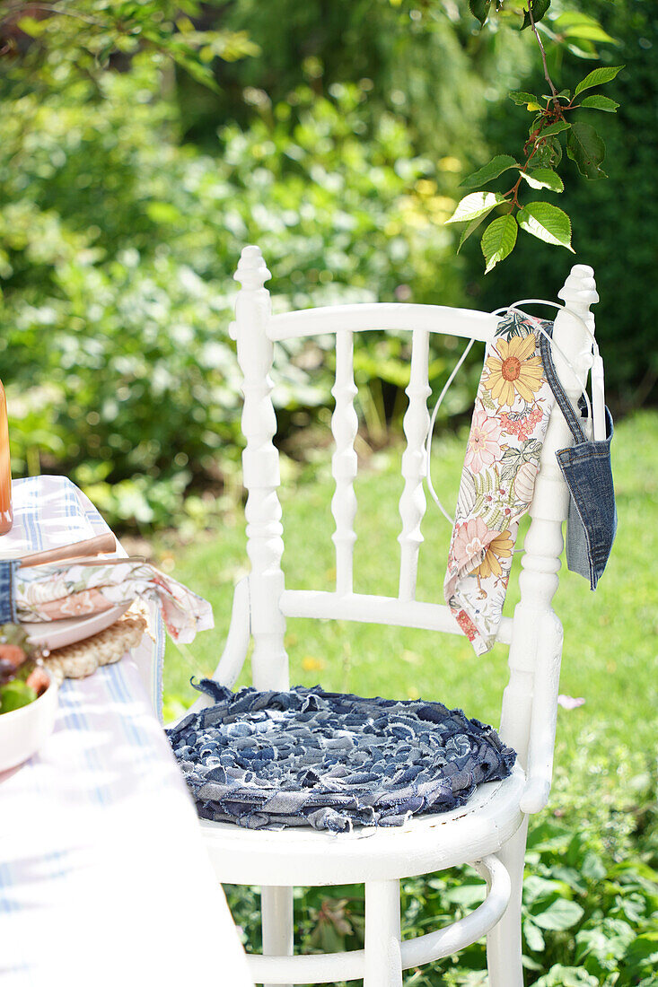 Weißer Holzstuhl mit Denim-Sitzkissen im sommerlichen Garten