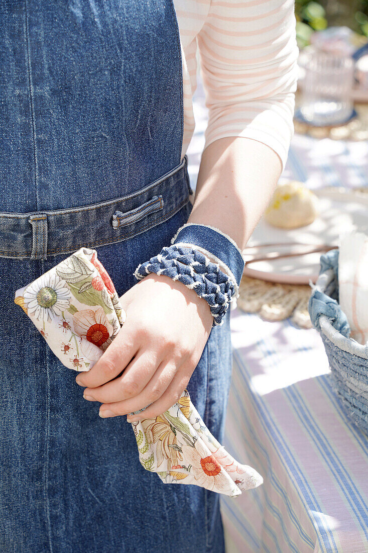 Person in denim apron and denim wristbands holding napkin with floral pattern