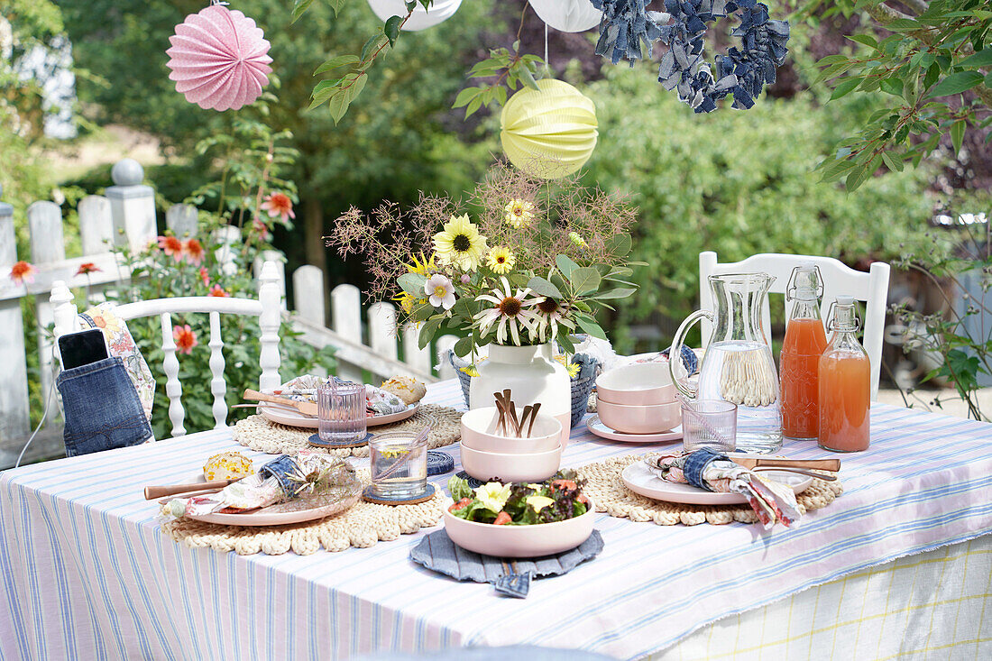 Gedeckter Tisch im Garten mit Blumenstrauß und Getränken auf gestreiftem Tischtuch