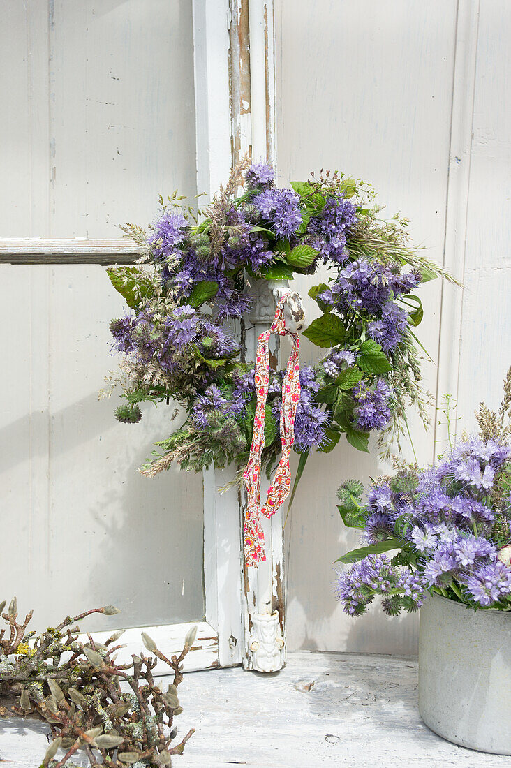 Meadow flower wreath of bee willow (Phacelia), grasses and shepherd's purse hanging from a window and bouquet of bee willow flowers