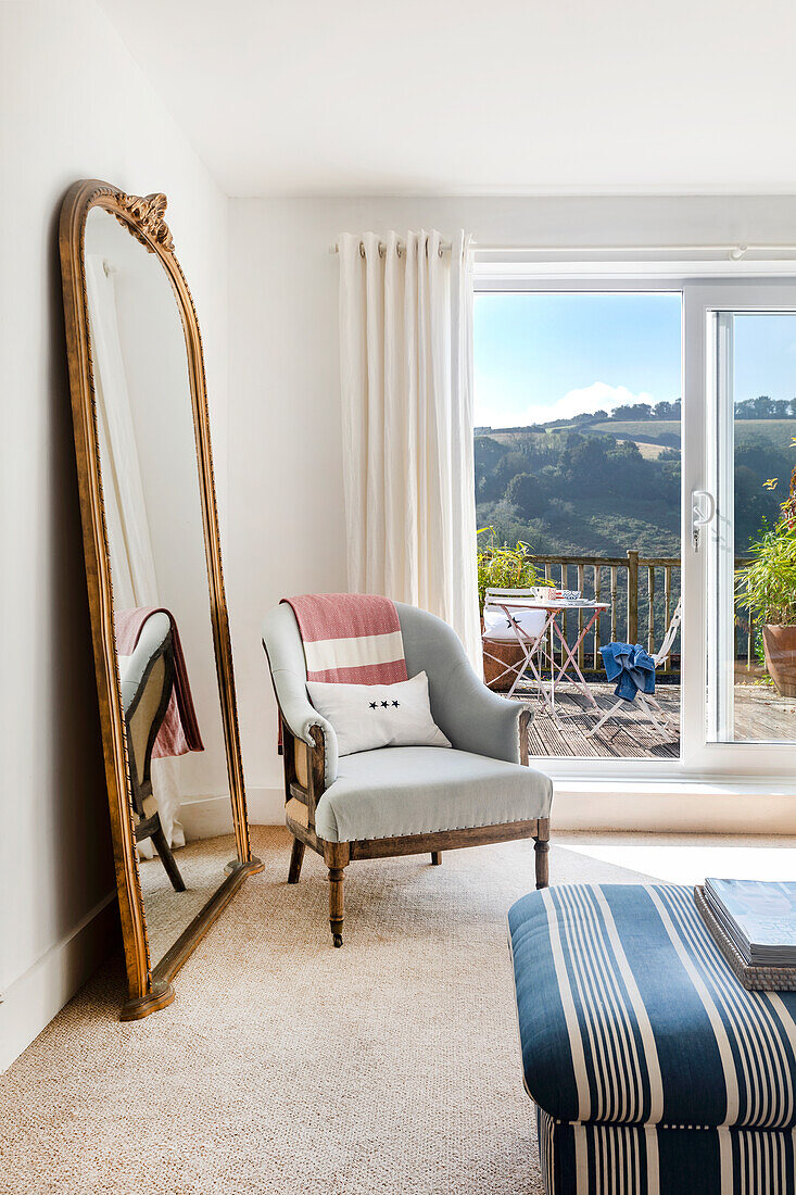 Armchair and large standing mirror in bright room with balcony access