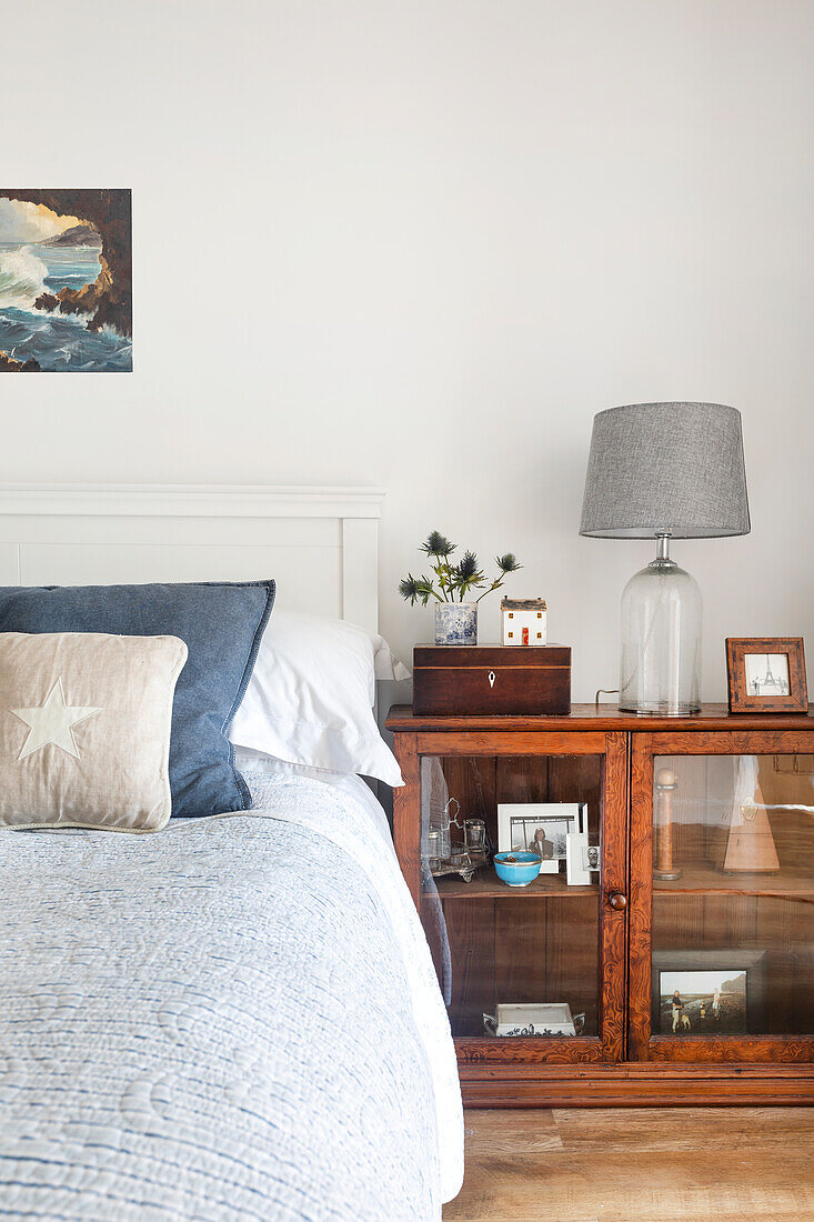 Bed next to cabinet with glass doors, glass lamp and decorative elements