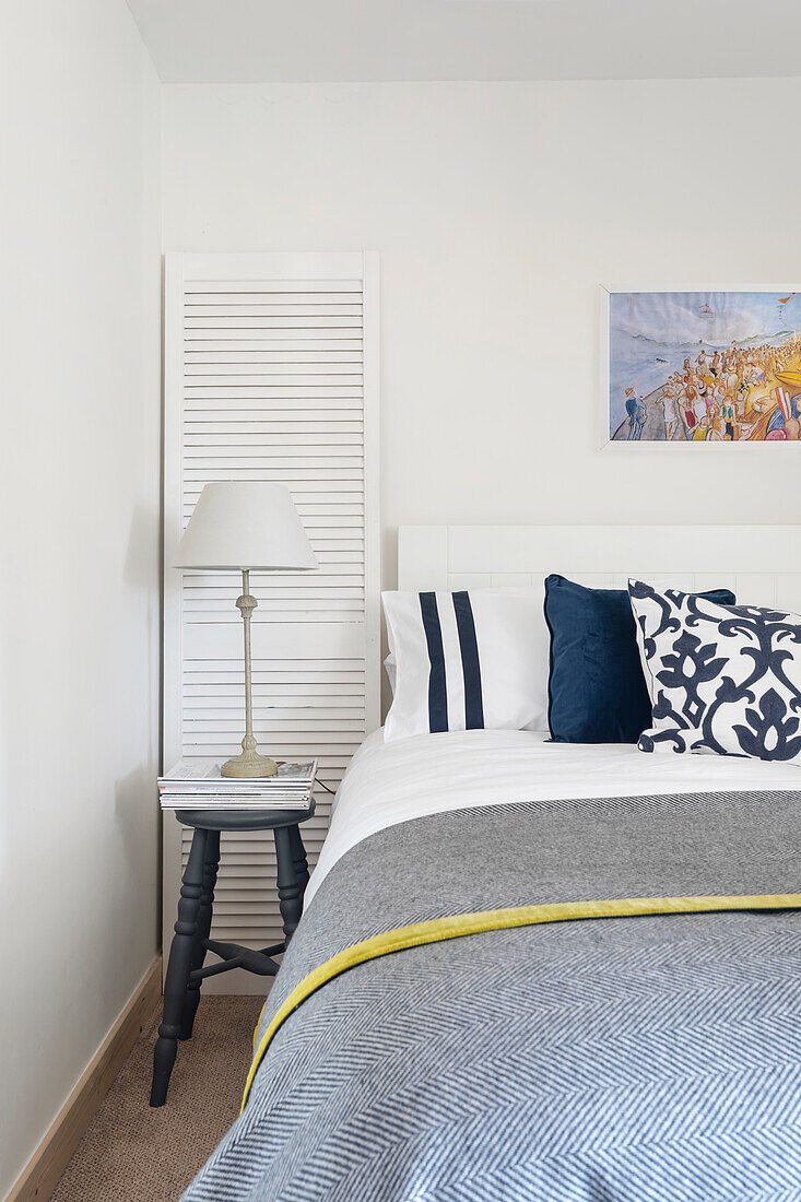 Bed with grey blanket and decorative pillows, bedside lamp and window shutter as decoration in the bedroom