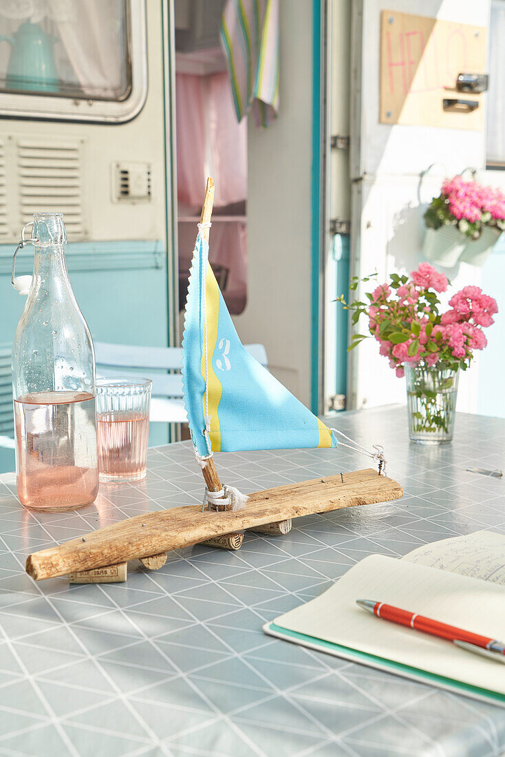 DIY-Holzsegelboot und Blumenvase auf Tisch vor Wohnwagen