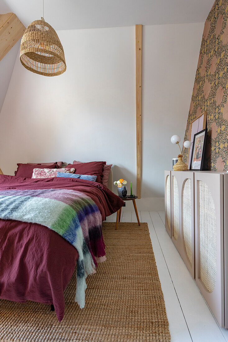 Bedroom with rattan lamp, patterned wallpaper and sisal carpet