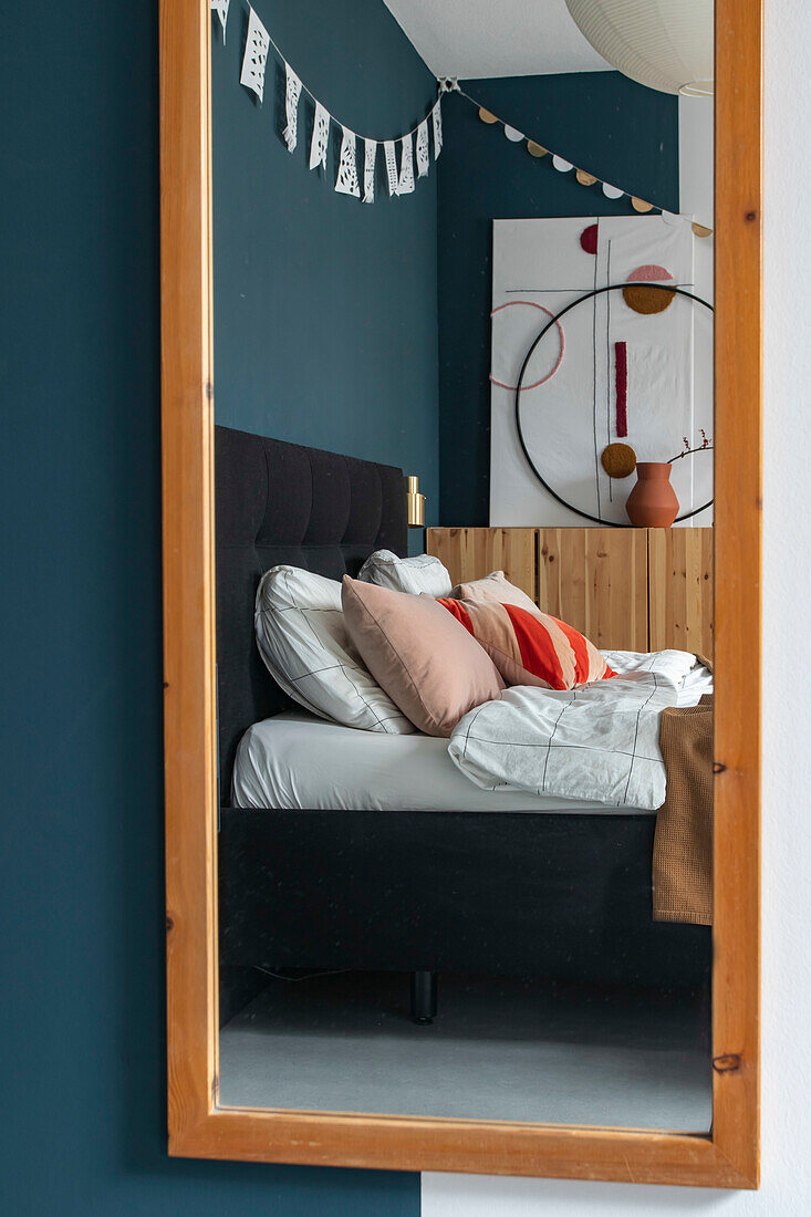 Mirror image of a bedroom with blue green walls and decorative throw pillows