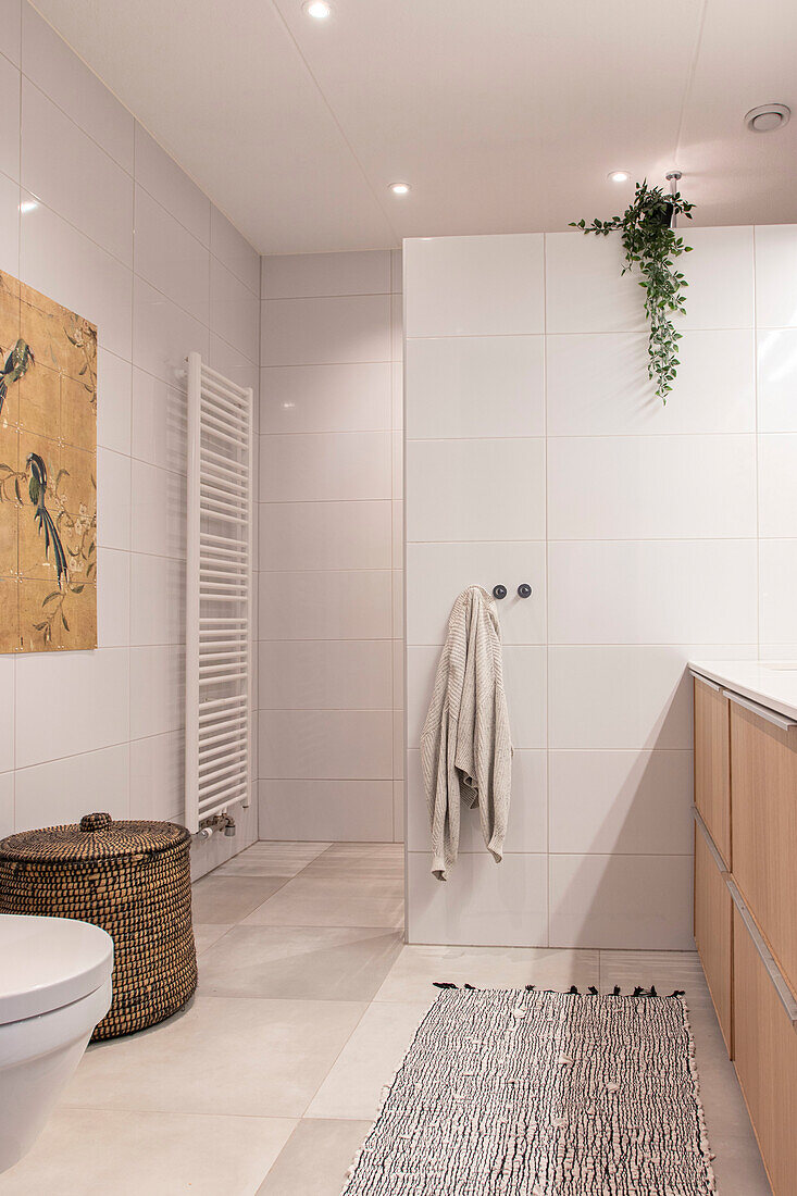 Modern bathroom with white tiled walls, light-colored wooden cabinet and woven laundry basket