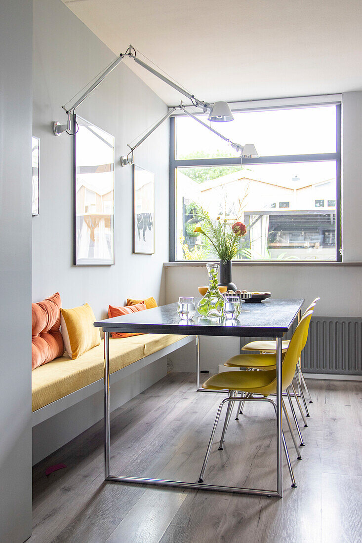 Dining area with yellow chairs and bench in bright room with large window