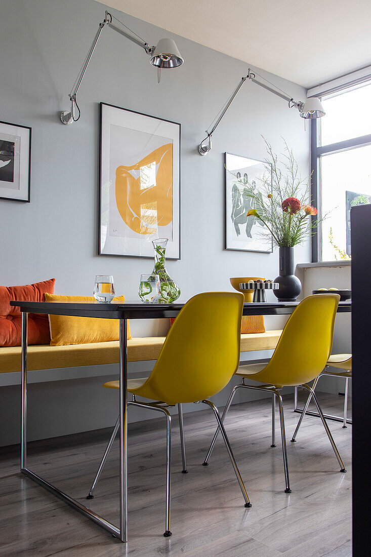 Dining area with yellow chairs and bench in front of light blue wall with artwork