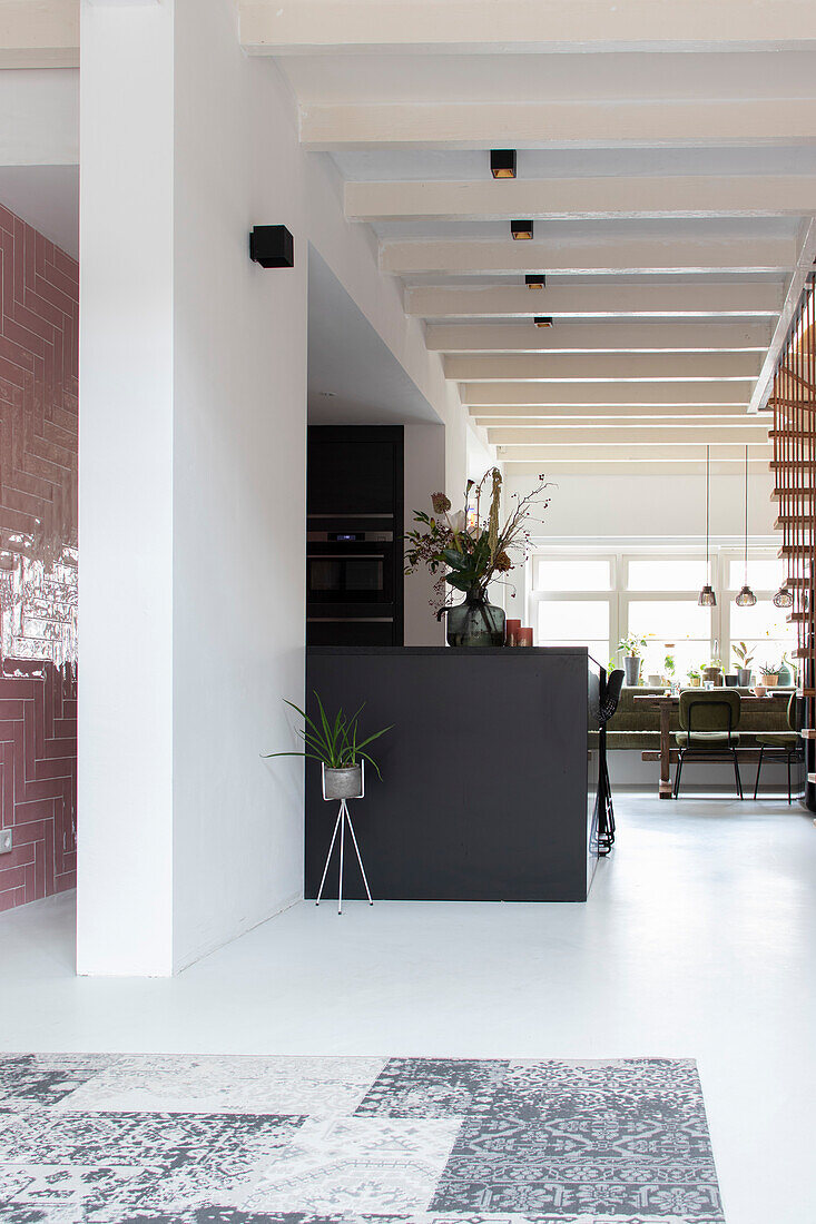 Modern kitchen with black cooking island and open-plan living area with white wooden beamed ceiling