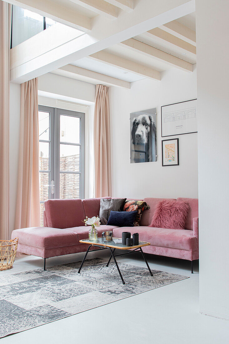 Living room with pink corner sofa, white-painted ceiling beams and pictures