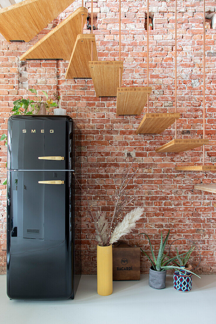 Black retro fridge in front of exposed brick wall with suspended wooden staircase