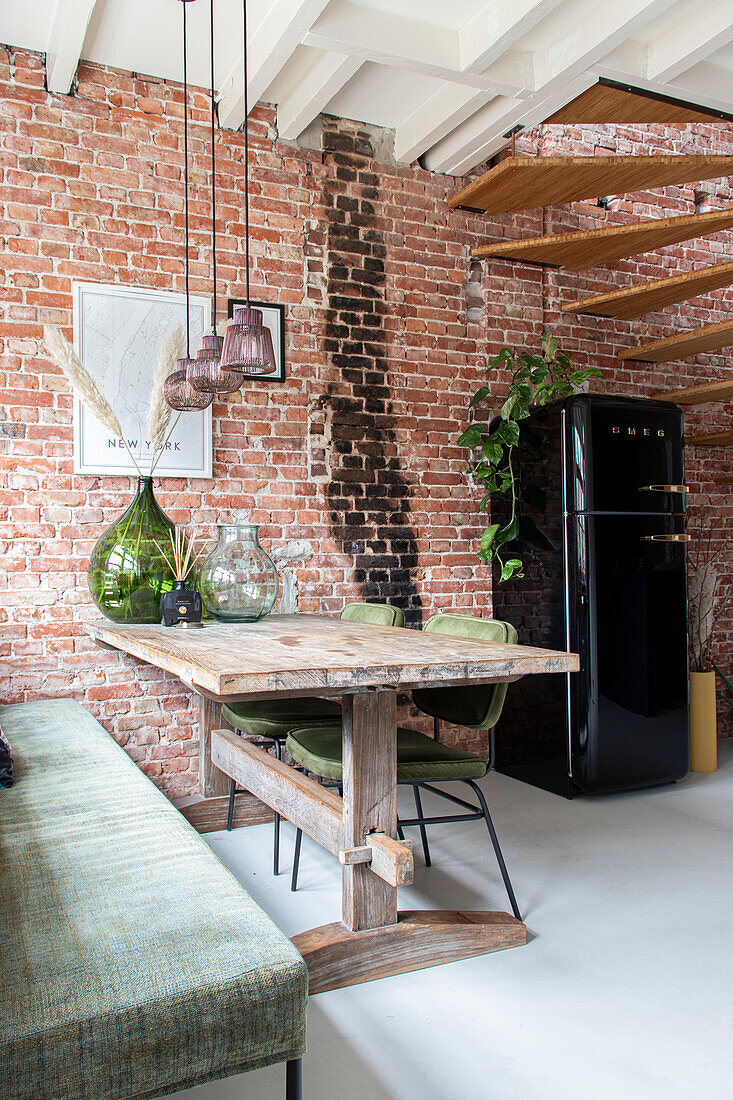 Dining area with rustic wooden table, brick wall and black retro fridge