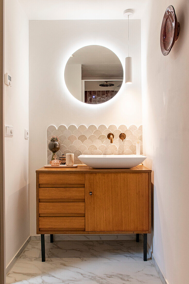 Modern bathroom with illuminated round mirror and wooden washbasin on marble floor