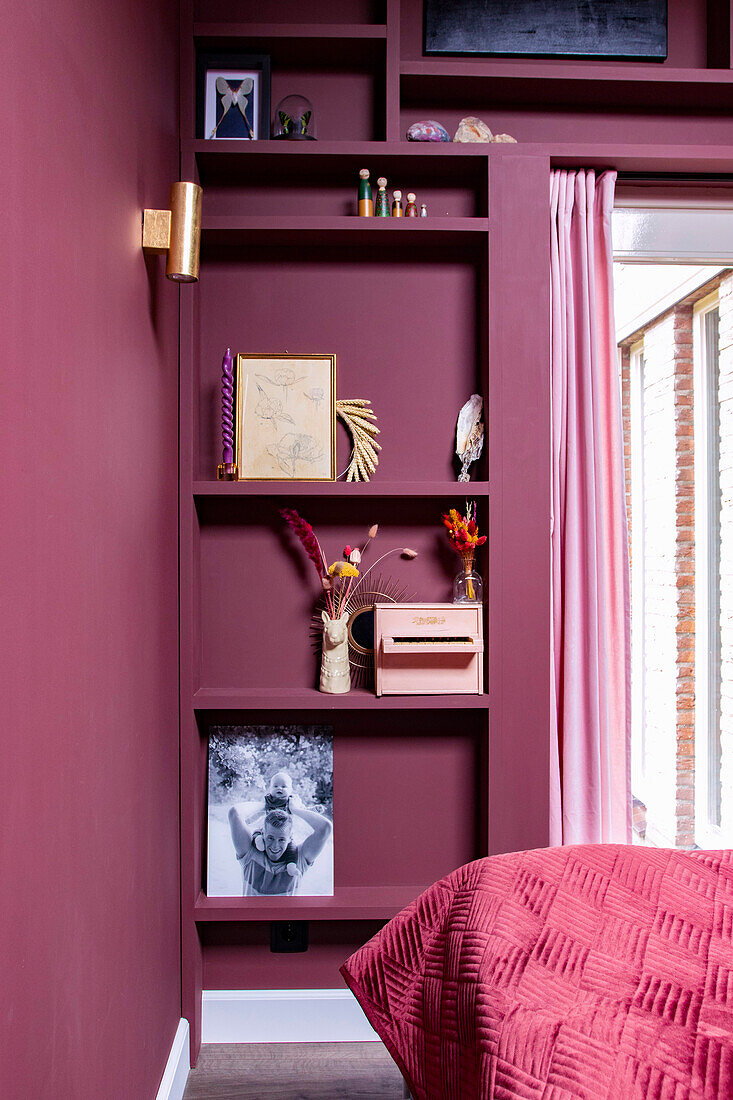 Built-in shelving in mauve-colored bedroom with decorative objects and dried flowers