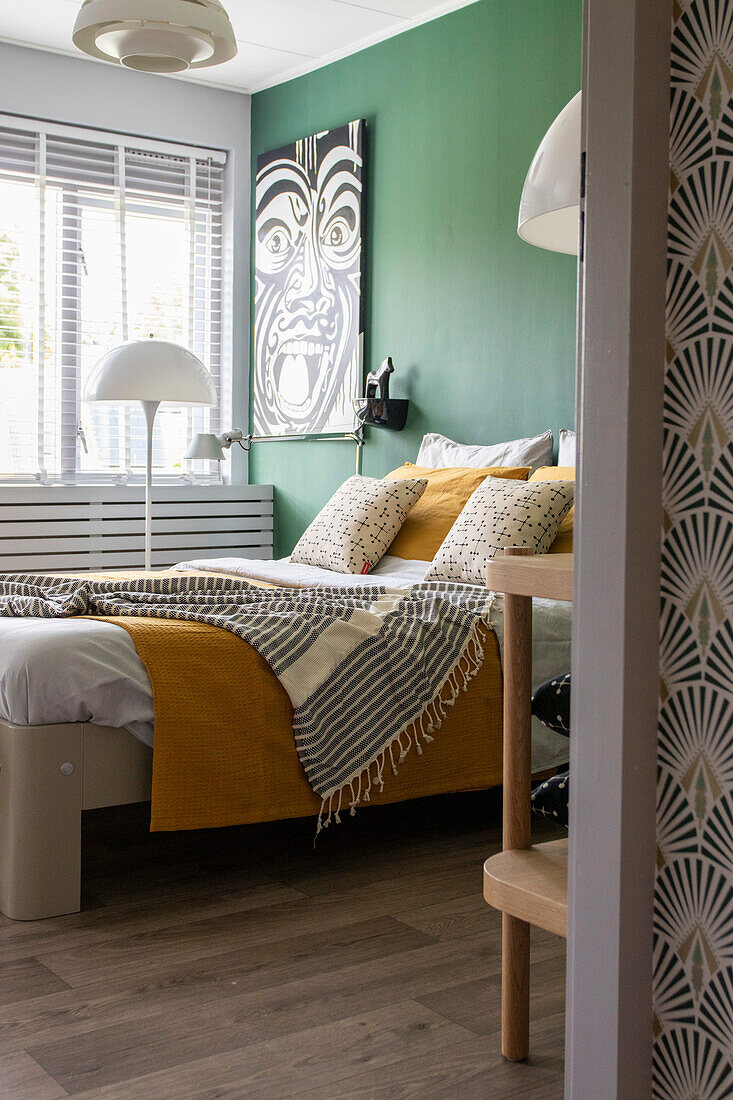 Bed in modern bedroom with green accent wall and wooden floor