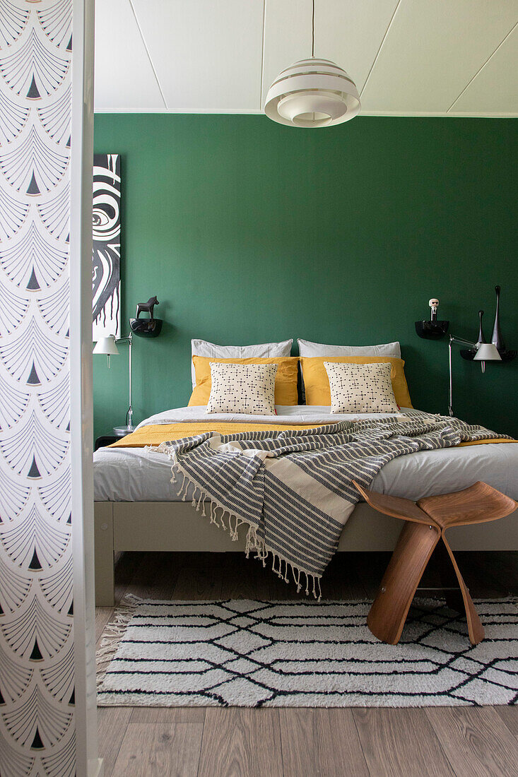 Bedroom with green-painted wall, double bed and modern wooden stool