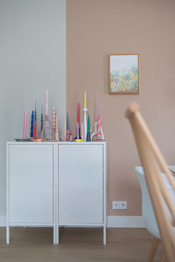 White cupboard with colorful candles and abstract picture on the wall