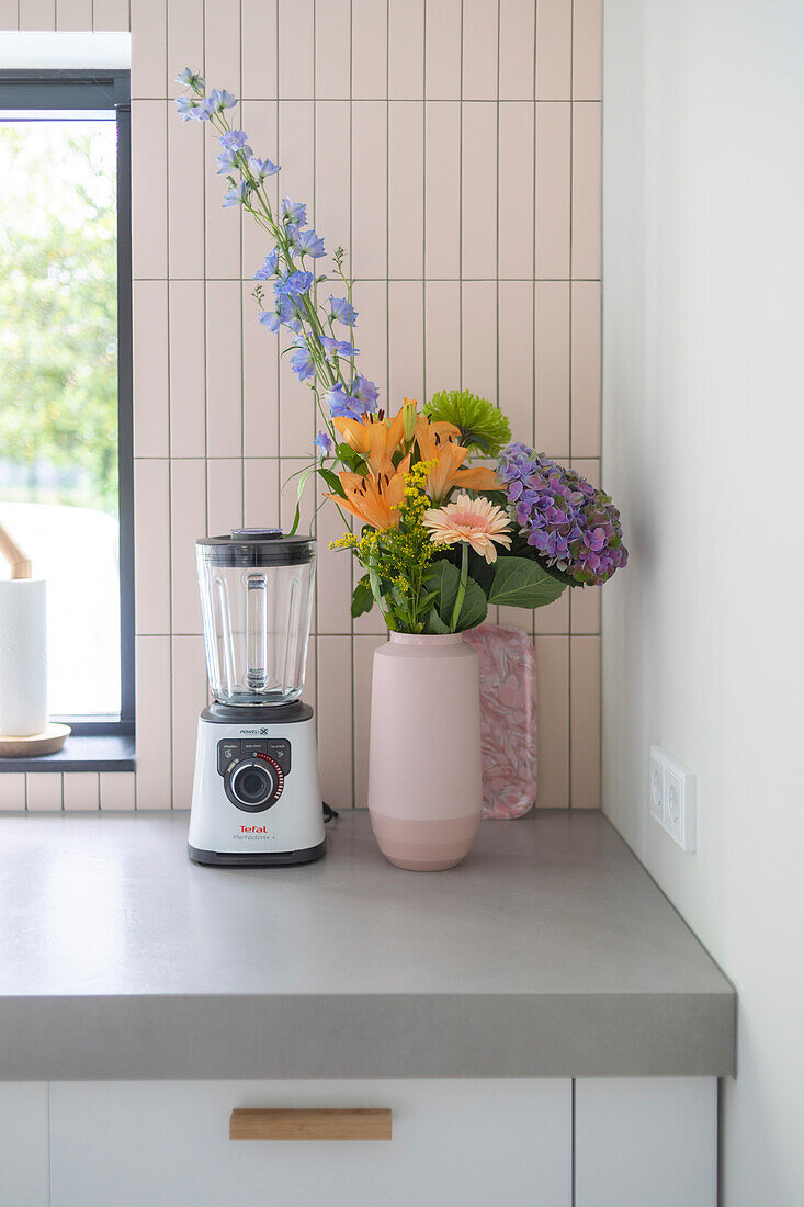 Bouquet of flowers in pink vase on kitchen counter next to blender