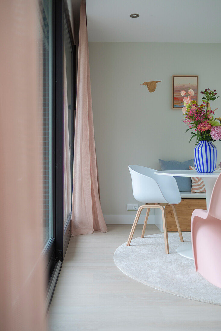 Bright dining area with round table and white chairs in front of floor-to-ceiling windows