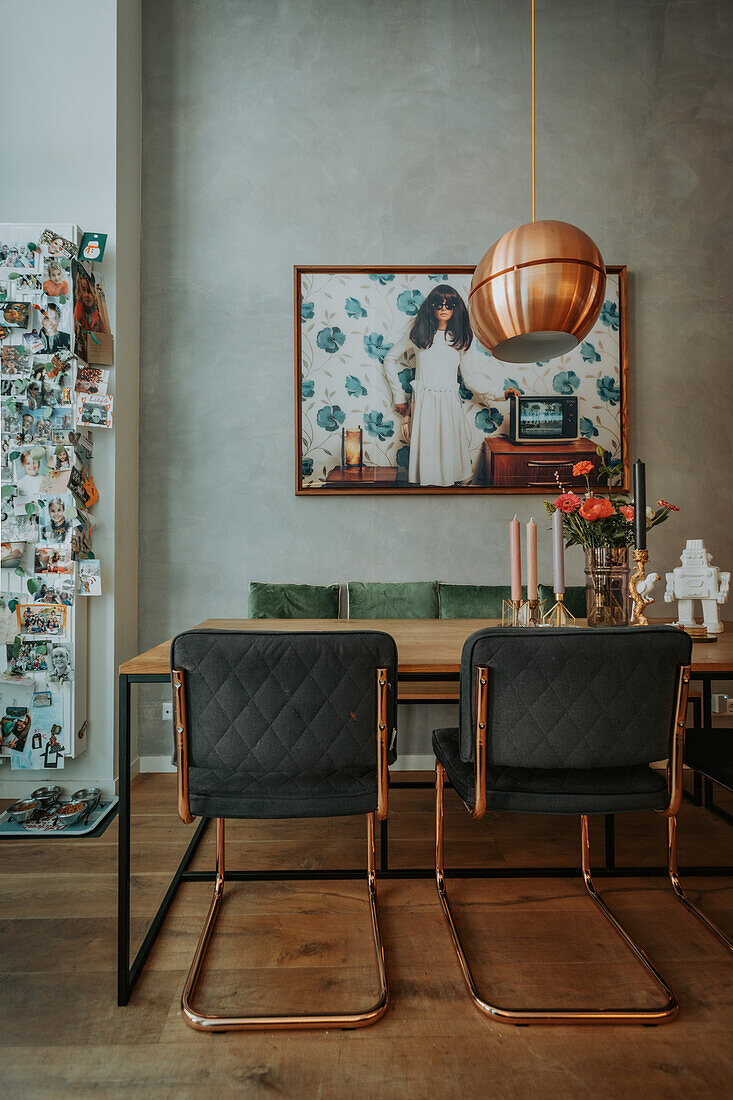 Dining area with copper-colored pendant light and upholstered chairs in front of grey wall with photo art