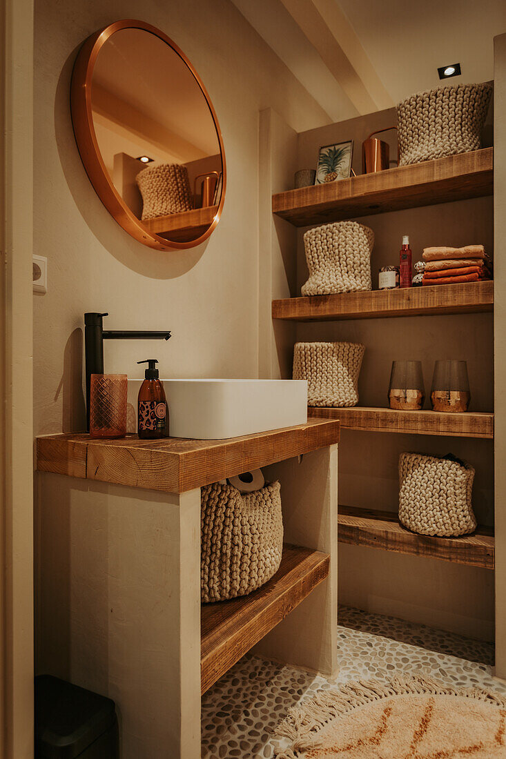 Small bathroom with wooden shelves and round copper mirror