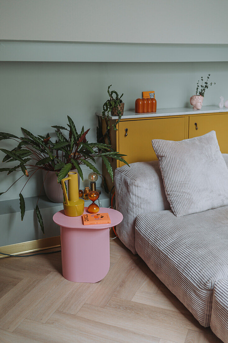 Wohnzimmer mit pastellrosa Beistelltisch, grauem Cord-Sofa und gelbem Sideboard