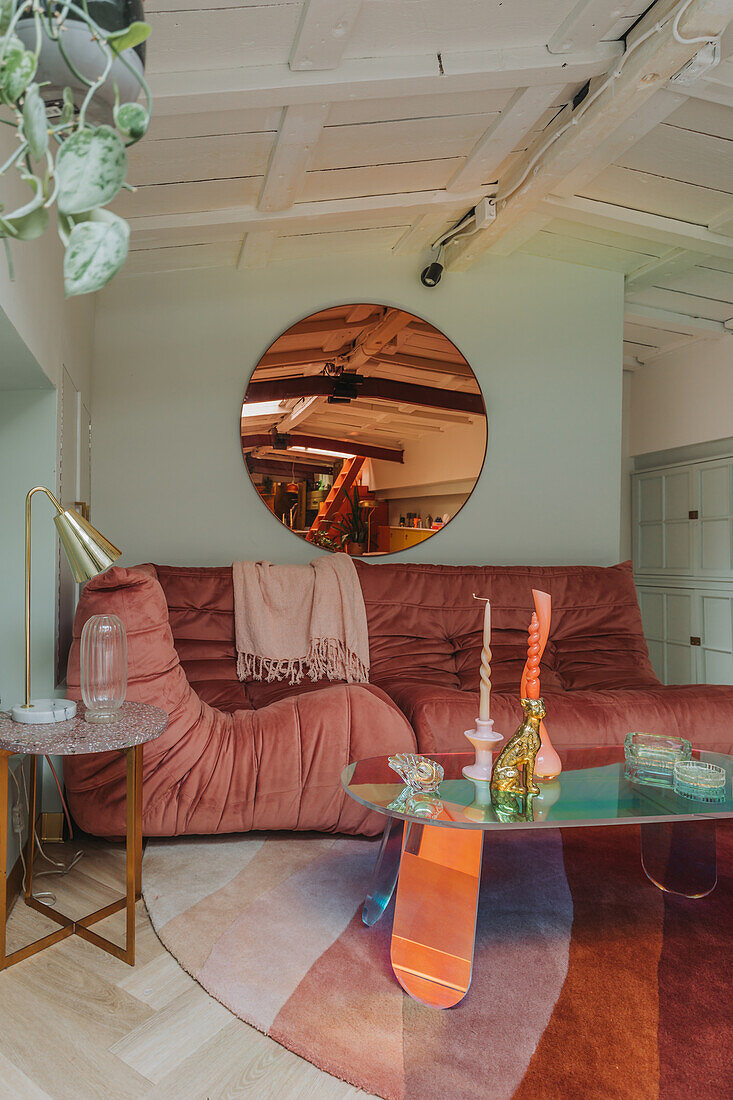 Pink velvet sofa with unusual glass table and round mirror in the living room