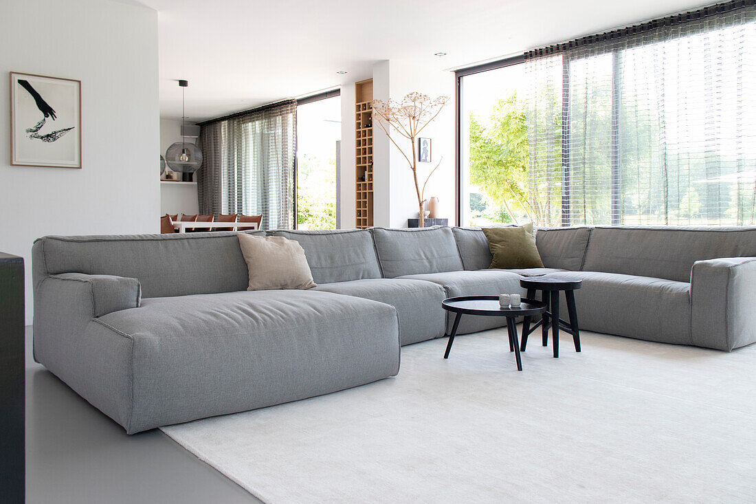 Grey corner sofa and round side tables in modern living room with large window front