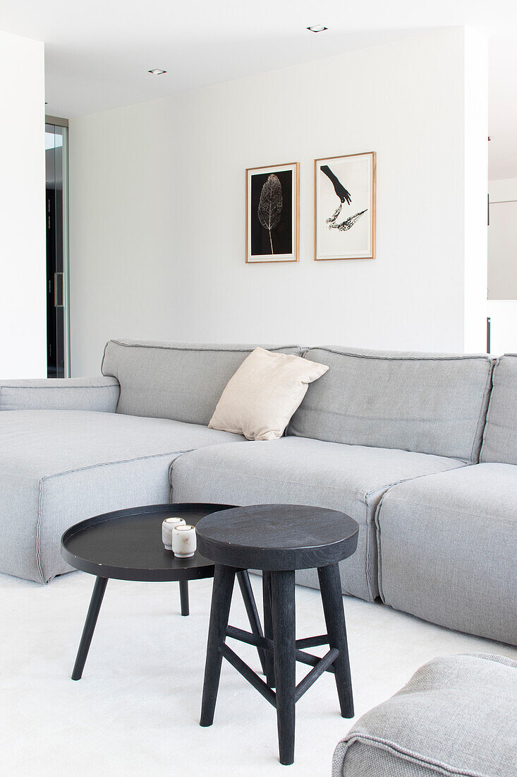 Grey corner sofa in the living room with round side table and black stool