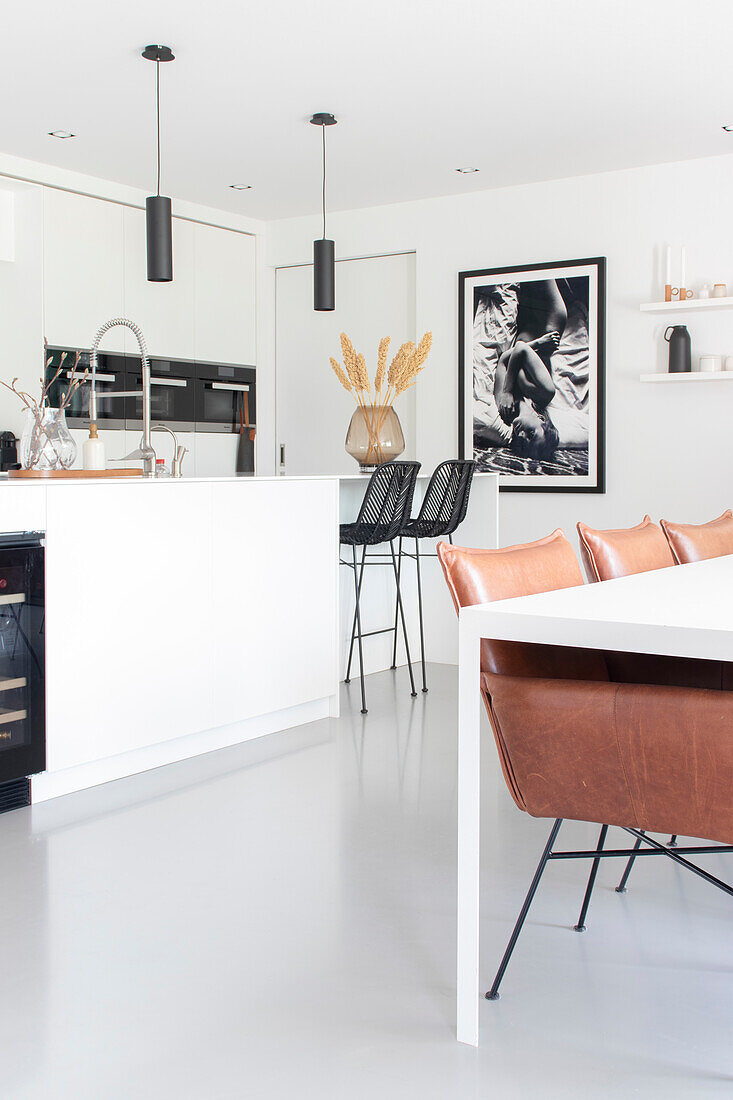 Modern white kitchen with black stools, leather chairs and black and white photography on the wall