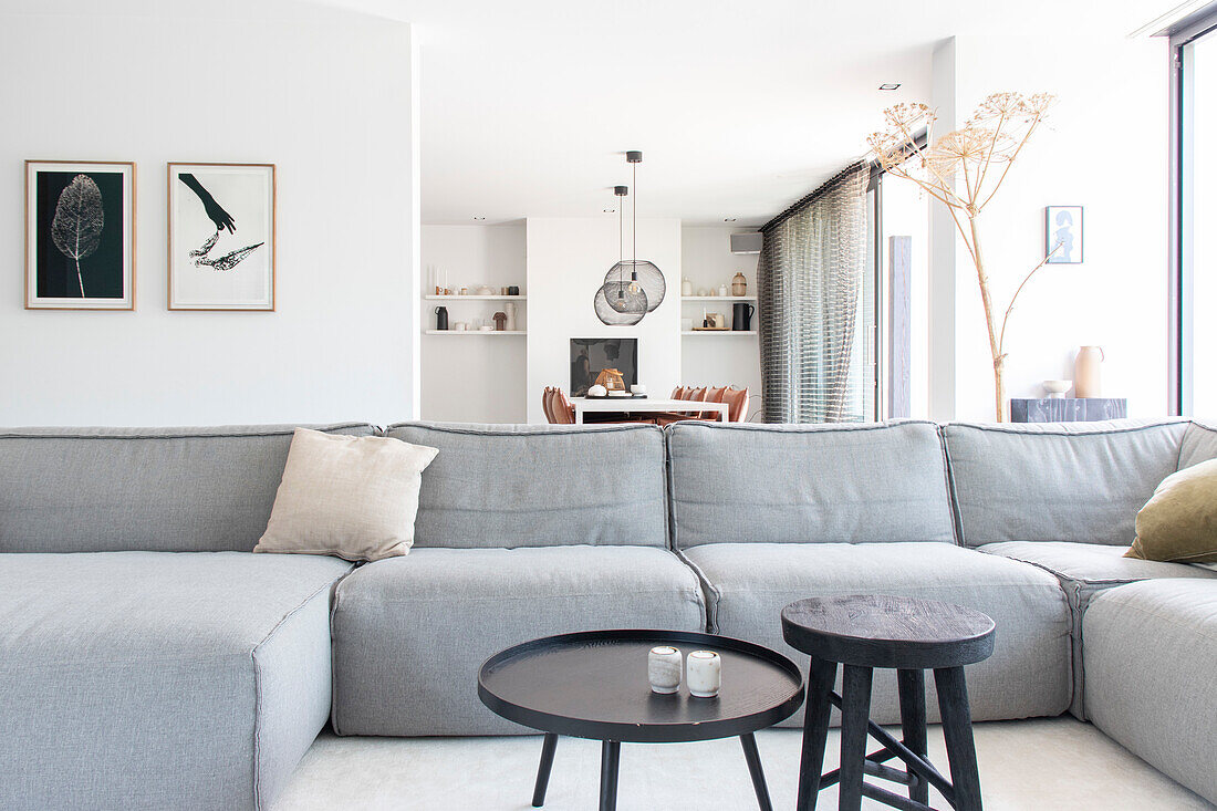 Large grey sofa and dark coffee tables in modern living room with open dining room in the background