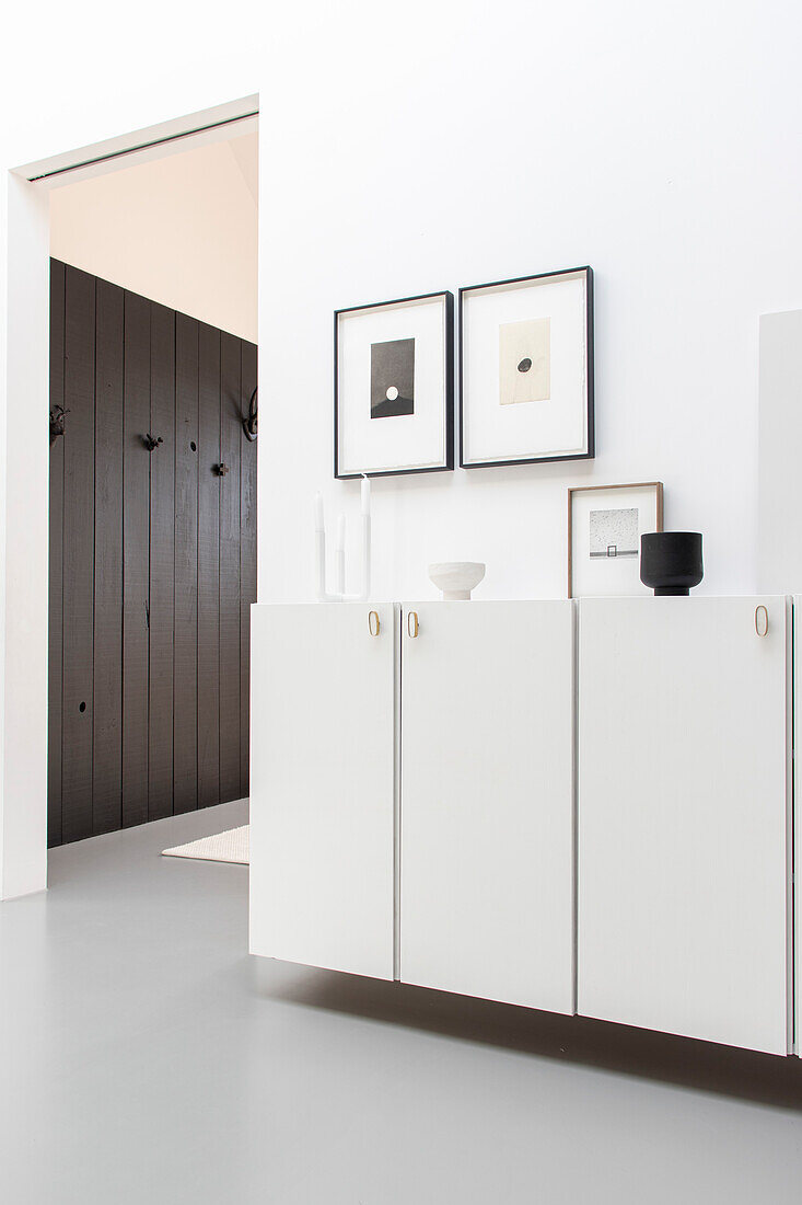 White wall cabinet with minimalist artwork and vases in modern hallway