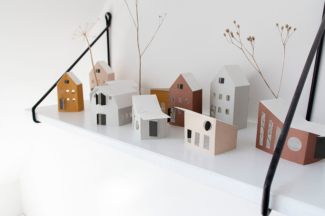 Paper houses and dried flowers on a white shelf