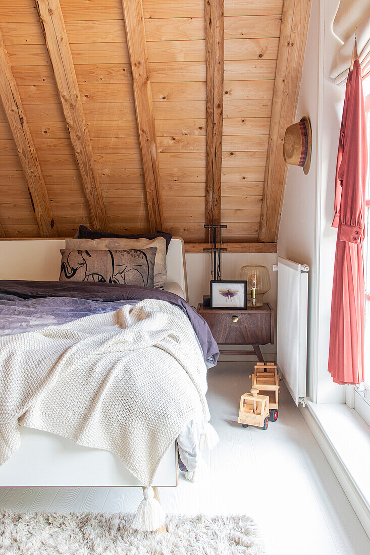 Attic bedroom with wooden beamed ceiling, bed and toy trolley