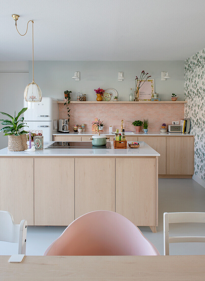 Open-plan kitchen with cooking island, pink backsplash and light-colored wooden cabinets