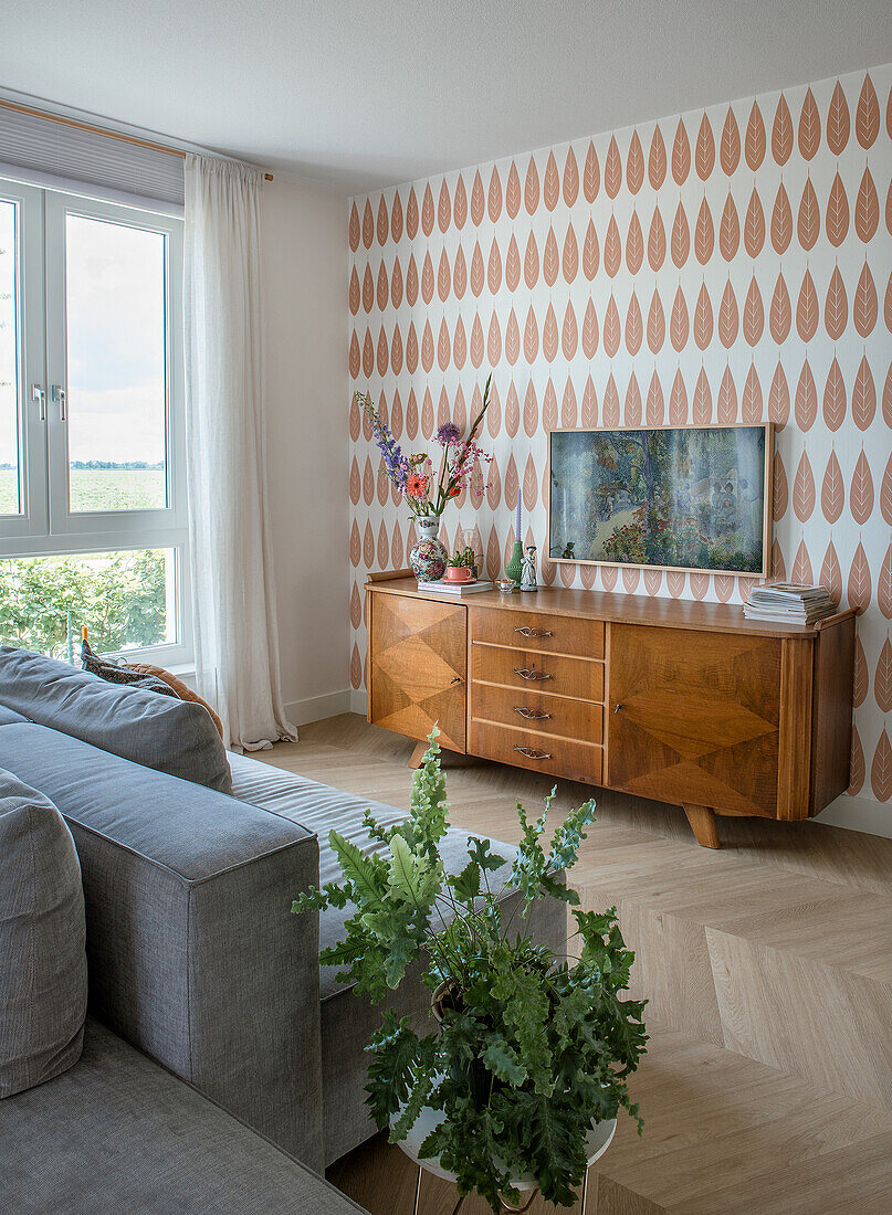 Living room with retro sideboard, herringbone parquet flooring and patterned wallpaper