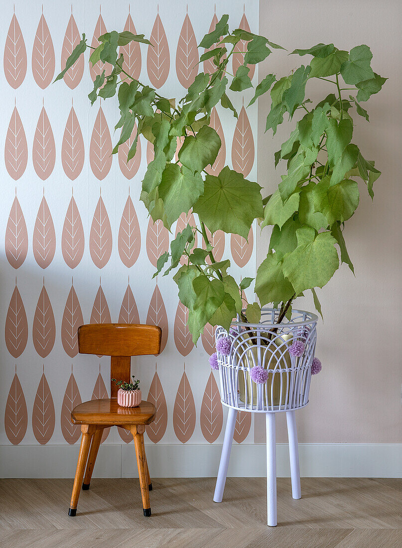 Potted plant in white metal stand and wooden chair in front of pastel-colored patterned wallpaper