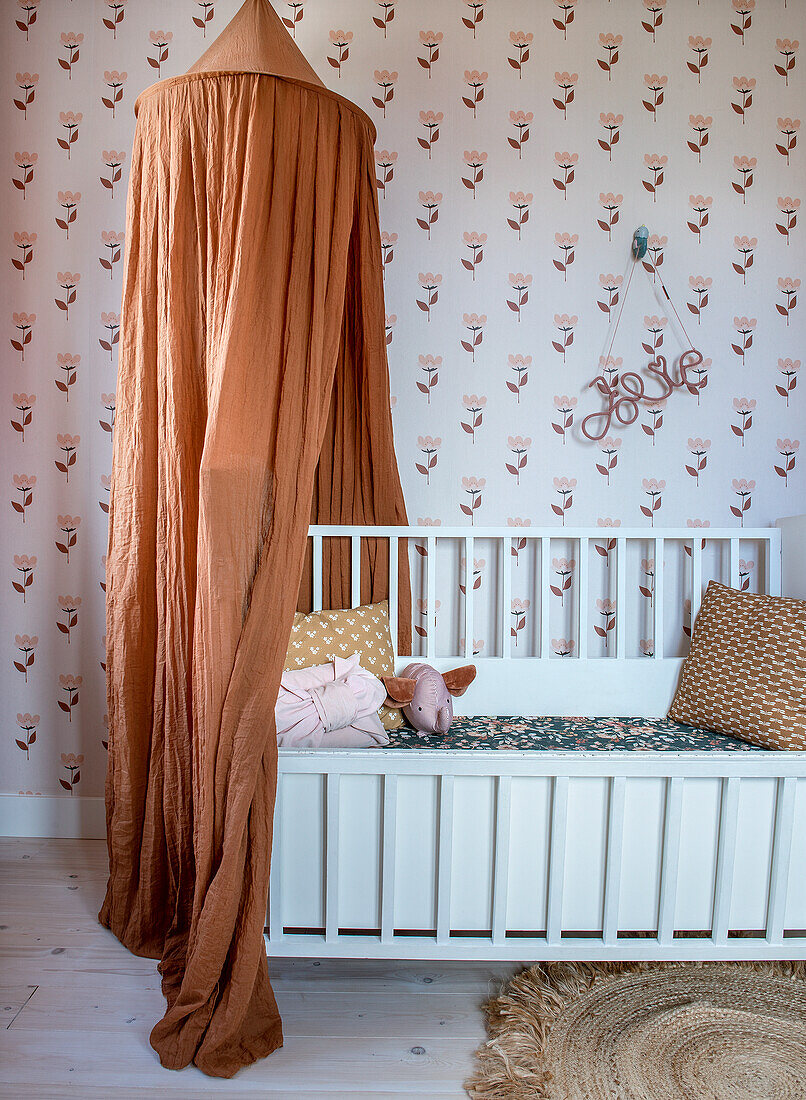 Gitterbett mit orangefarbenem Baldachin im Babyzimmer mit Blumen-Tapete