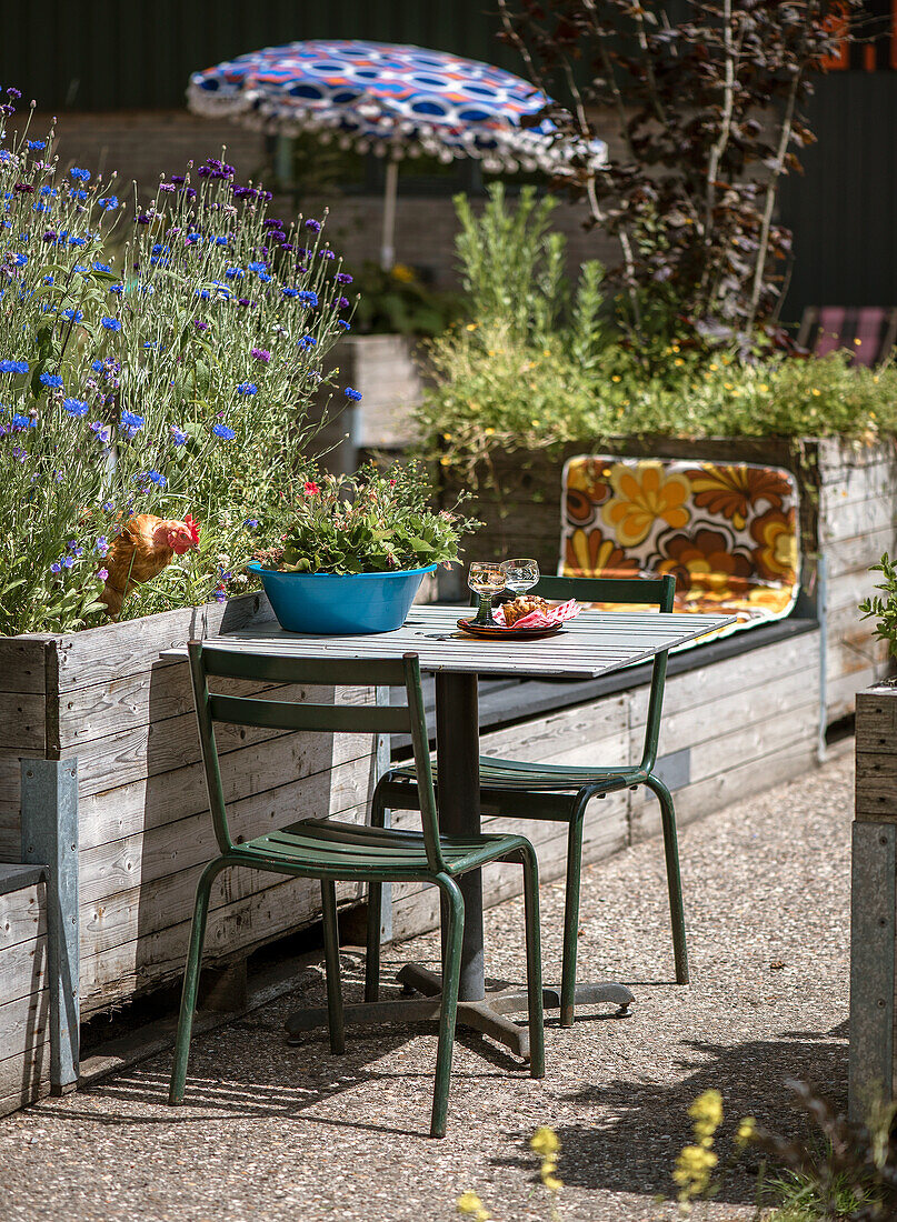 Kleiner Sitzbereich mit Metallstühlen und blühendem Hochbeet im Garten