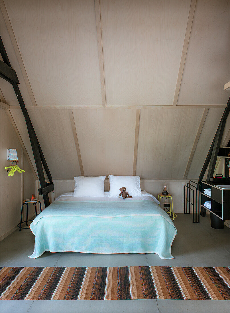 Double bed with turquoise bedspread and striped carpet in bedroom under sloping ceiling