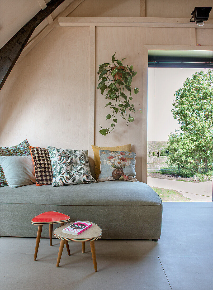 Modern living room with grey sofa and vintage stools, open door to the garden