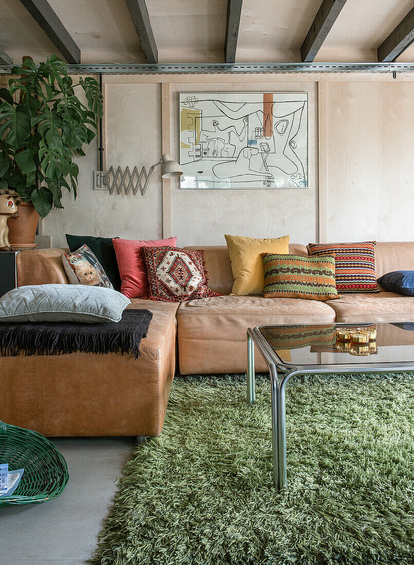 Living room with leather sofa, colorful cushions and green deep-pile carpet