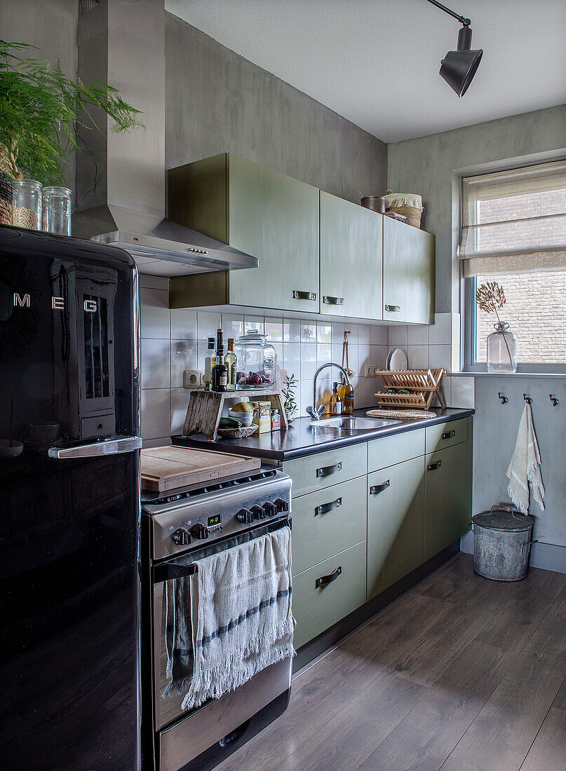 Kitchen with green cupboards and black retro fridge