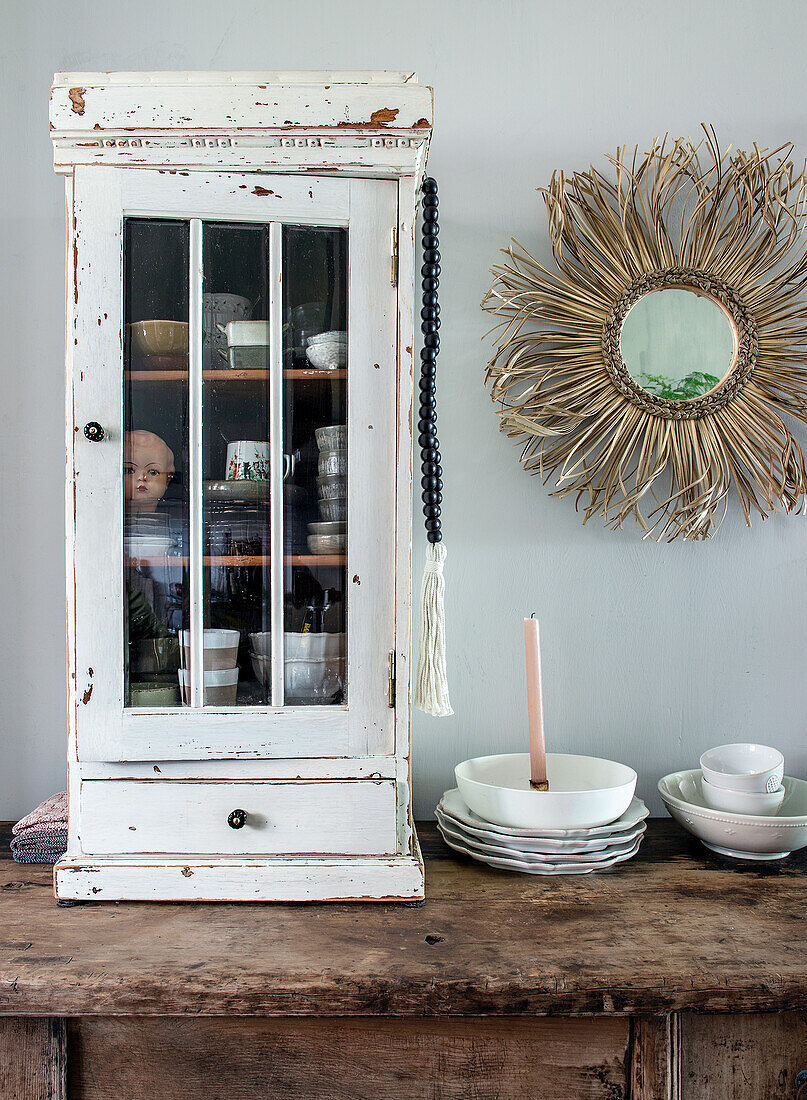 Vintage kitchen cupboard with crockery next to rustic mirror and candle