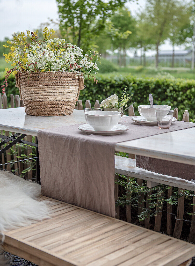 Gedeckter Gartentisch mit Blumenarrangement in einem Korb